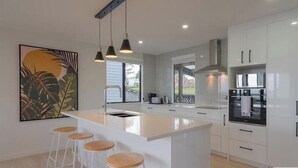 A modern kitchen with white cabinetry, a central island with stools, pendant lighting, and a large window providing natural light.