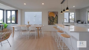 A modern kitchen with a central island, white bar stools, and a dining area with a table and chairs.