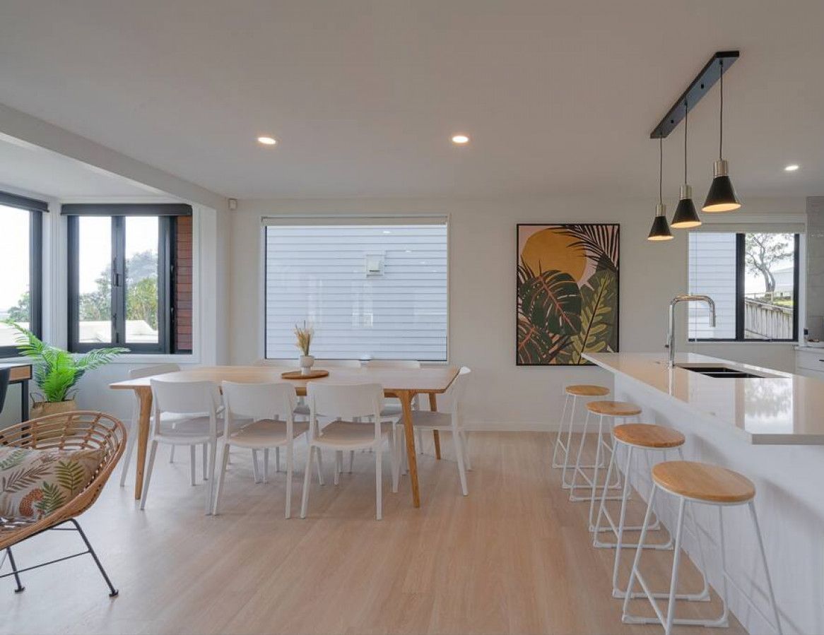 A modern kitchen with a central island, white bar stools, and a dining area with a table and chairs.