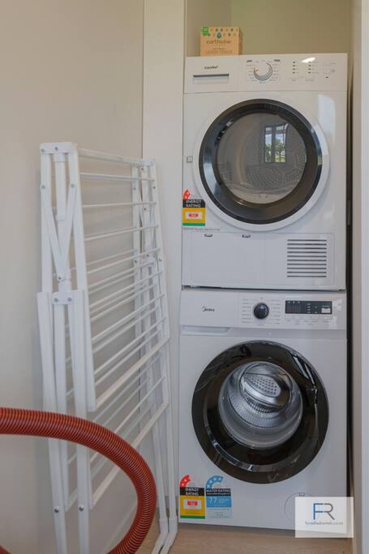A front-loading washer and dryer unit with a drying rack to the left.