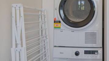 A front-loading washer and dryer unit with a drying rack to the left.