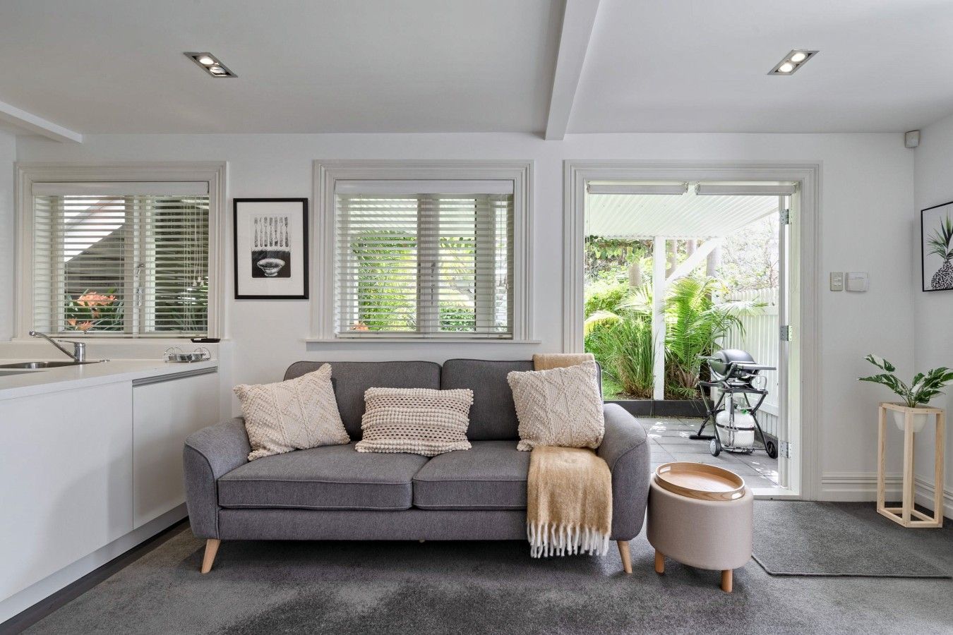 A modern living space with a grey sofa, a kitchen area, and a view of the outdoors.