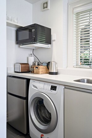 A compact kitchen with a built-in microwave, a toaster, a kettle, and a washing machine. - Delightful Freemans Bay Home|by Furnished Rentals (Auckland)