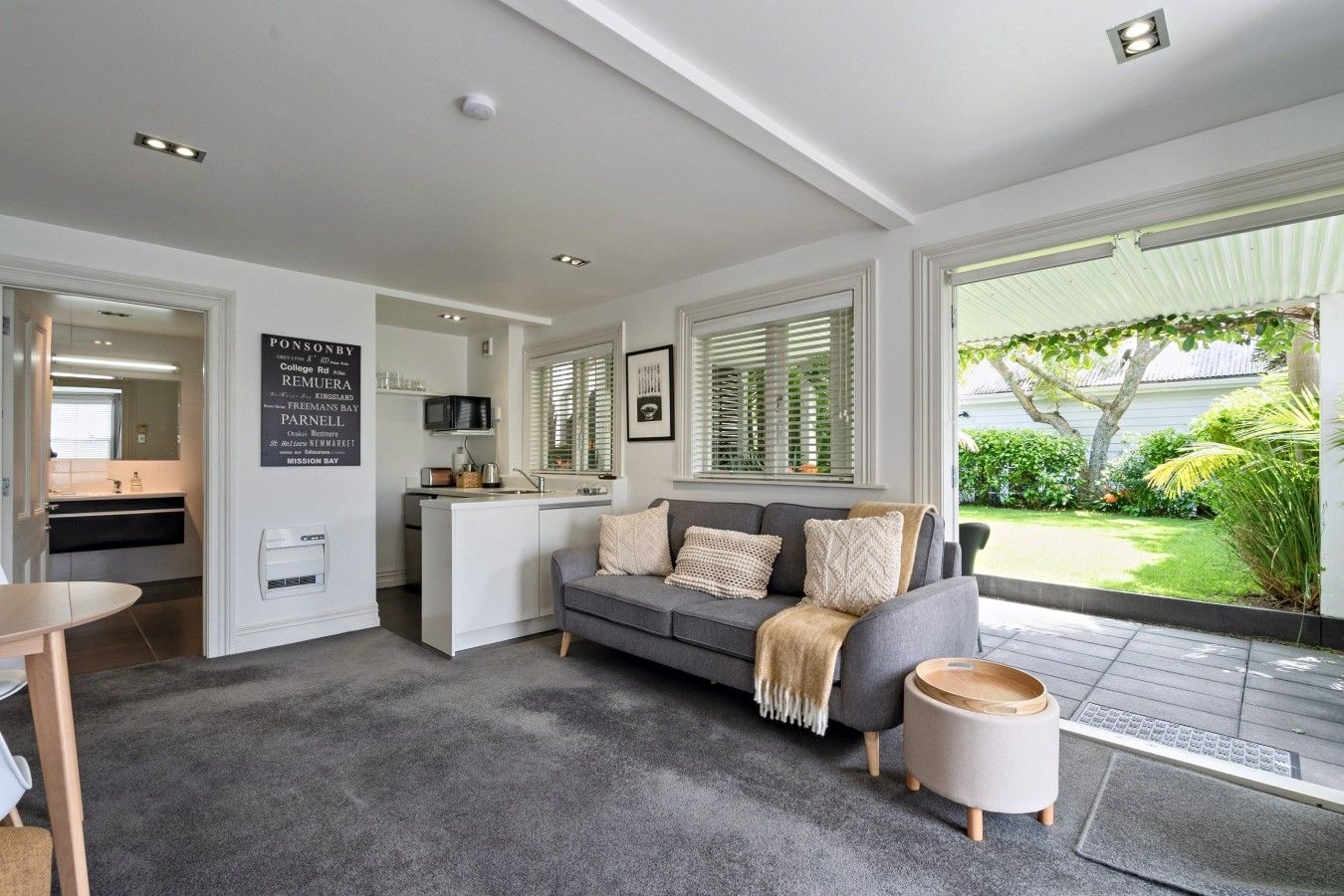 Een modern interieur met een grijze bank, een klein rond tafeltje en een keukenhoek.