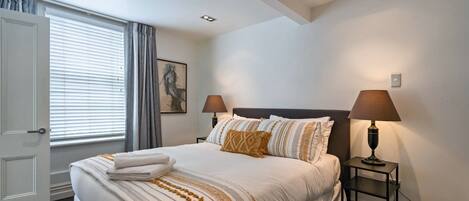 A hotel room with a bed, two bedside lamps, a door, and a window with curtains.