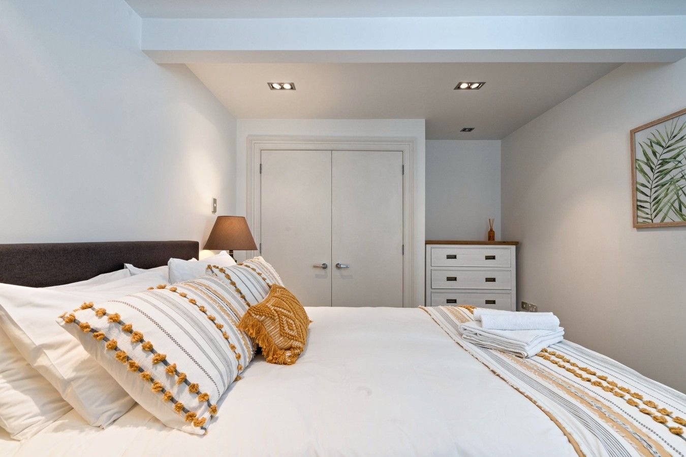 A bedroom with a bed, a nightstand, a lamp, a dresser, and a door.