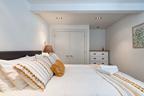 A bedroom with a bed, a nightstand, a lamp, a dresser, and a door. - Delightful Freemans Bay Home|by Furnished Rentals (Auckland)