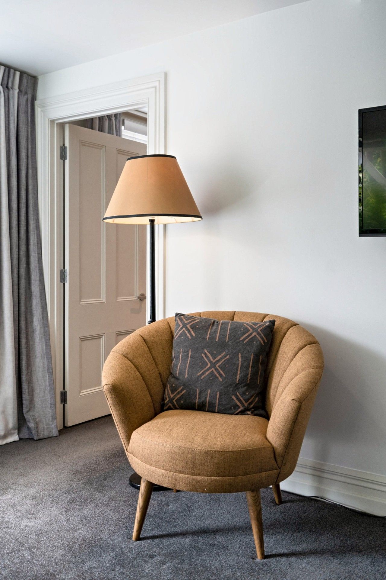 Ein Zimmer mit einem braunen Sessel, einer Lampe, einer Tür und einem an der Wand hängenden Bild.