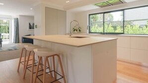 A modern kitchen with a central island, bar stools, a window with a view, and recessed ceiling lights. - Lux Living St Heliers|by Furnished Rentals (Auckland)