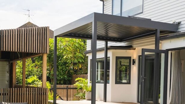 A modern outdoor patio with a covered seating area, a wooden fence, and a house in the background. - Lux Living St Heliers|by Furnished Rentals (Auckland)