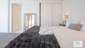 Ein Hotelzimmer mit einem Bett, einem Nachttisch mit Lampe und Blick ins Freie durch eine Tür.