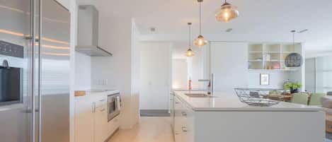 Une cuisine moderne dotée d’un îlot central, de luminaires suspendus et donnant sur l’espace de vie.