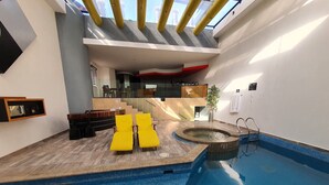 A modern indoor swimming pool with a sunroof, a small hot tub, and a seating area with yellow chairs. - Hotel Alcampo  (El Marques)