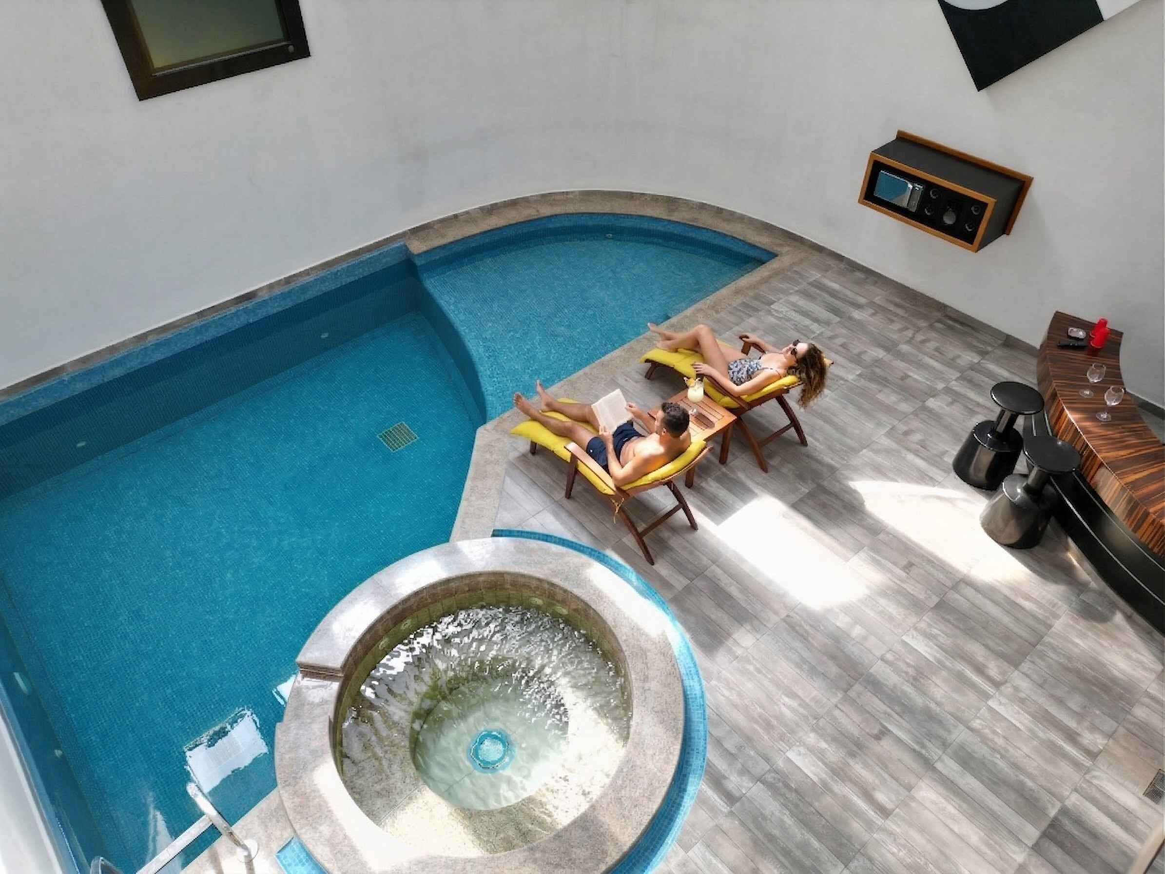 A swimming pool with two sun loungers and a hot tub.