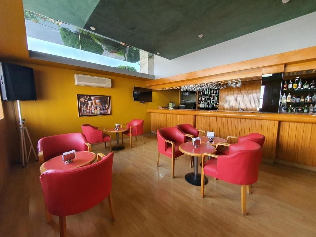 A bar area with a wooden counter, red chairs, and a bar stocked with bottles.