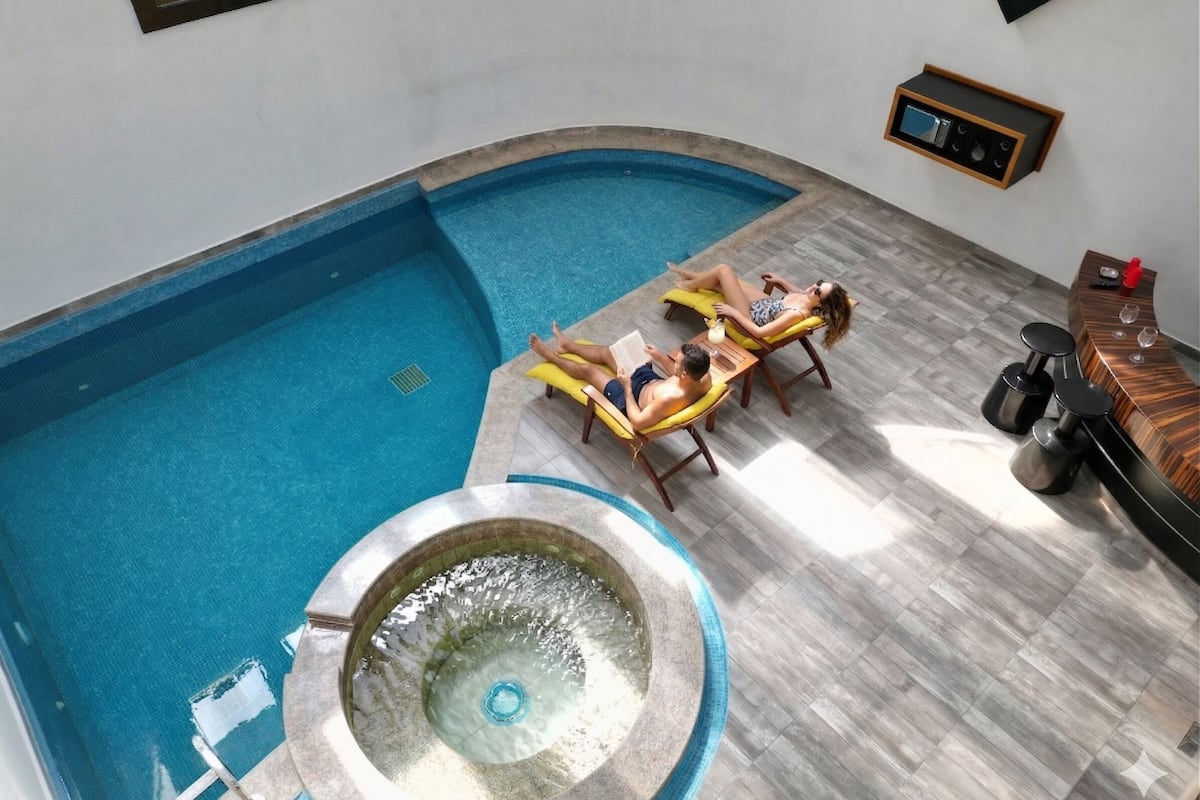 A swimming pool with lounge chairs, a hot tub, and a bar area.
