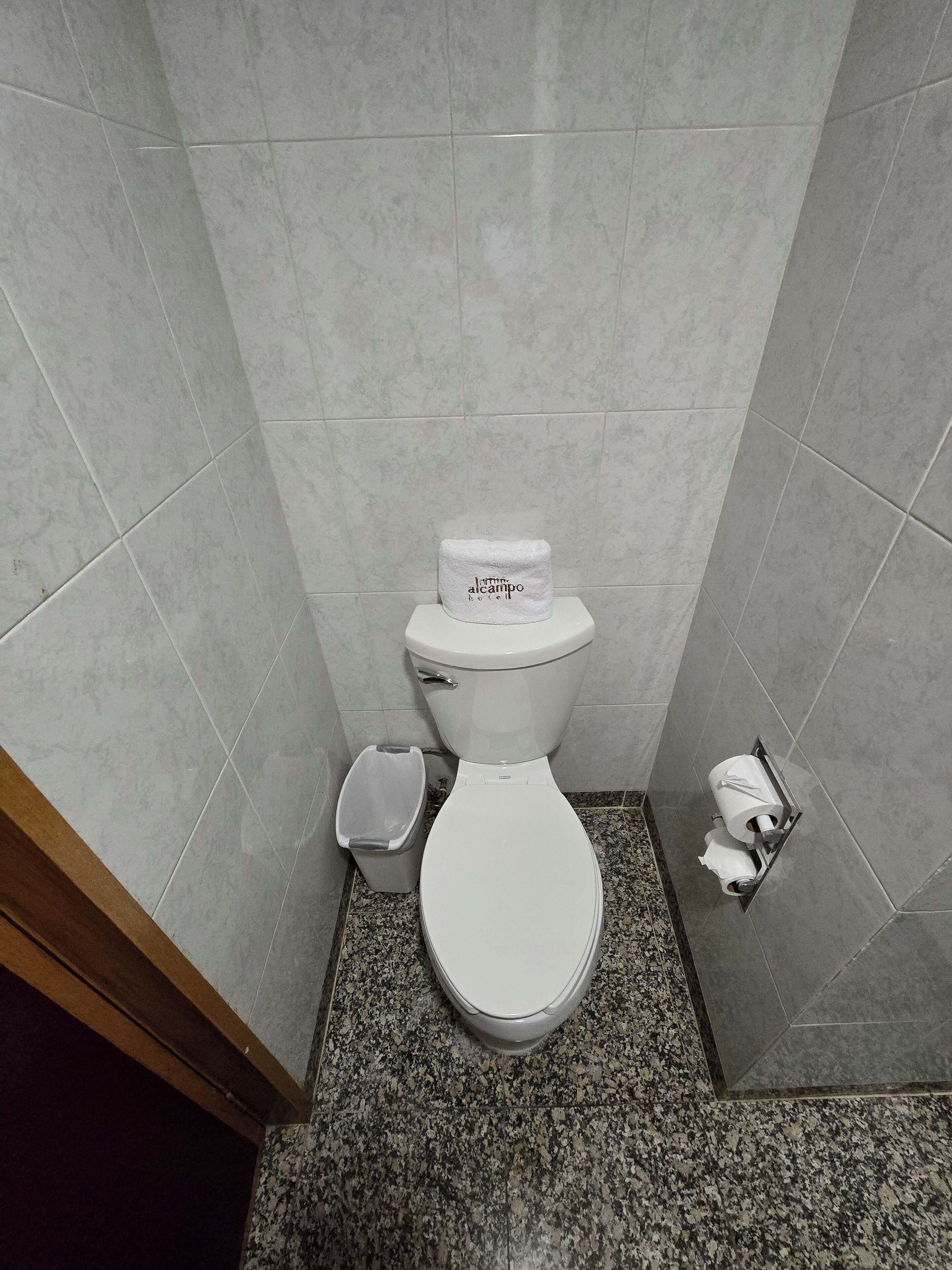 A small, clean bathroom with a toilet, a trash bin, and a toilet paper holder.
