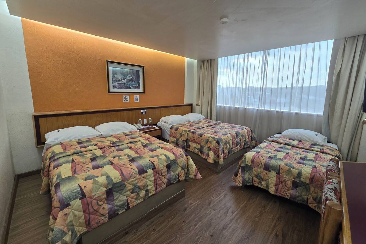 A hotel room with two beds, a wooden headboard, a painting on the wall, a window with curtains, and a wooden floor.