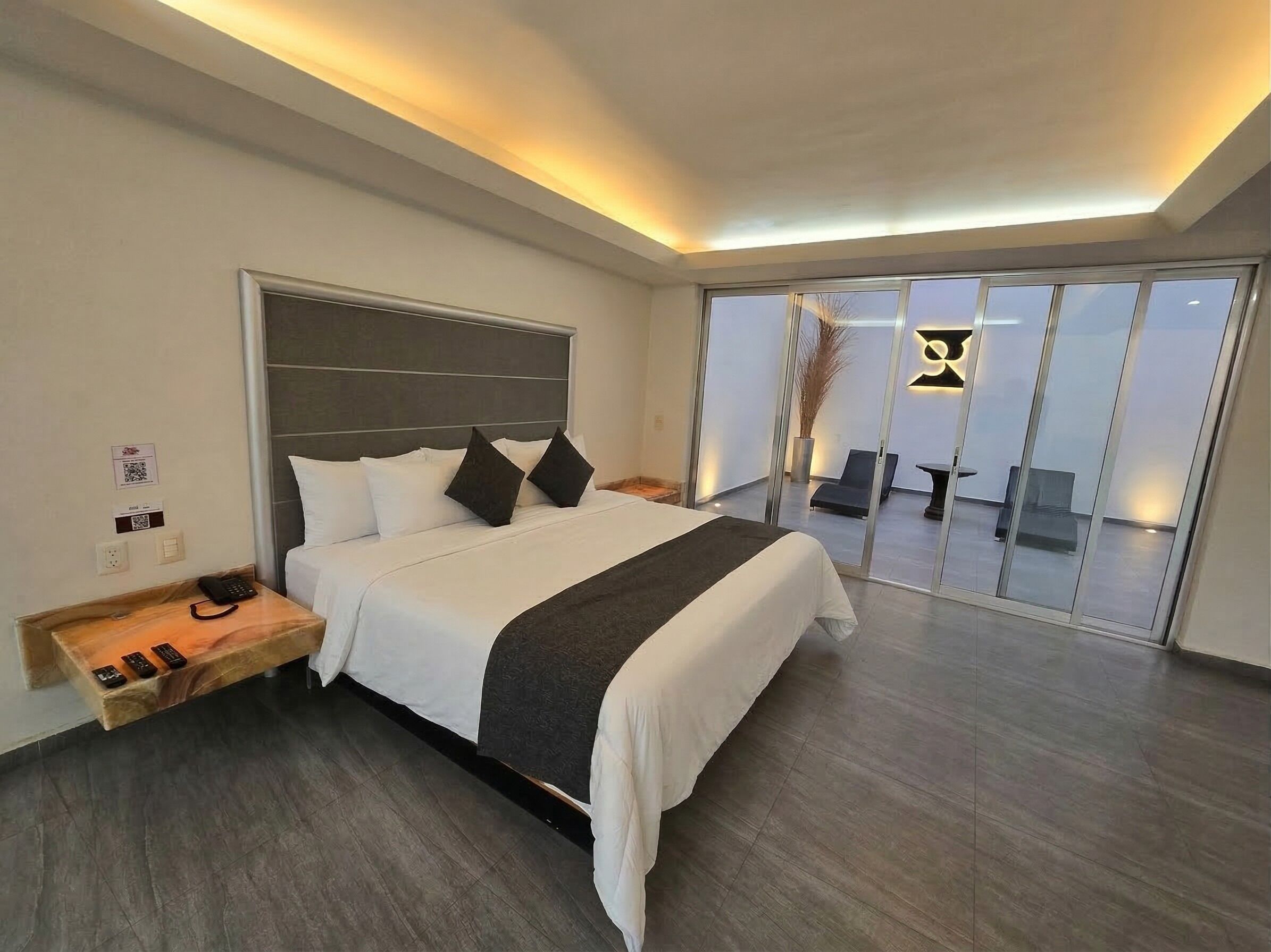 Camera d'albergo moderna con un letto grande, un comodino con il telefono e una porta scorrevole in vetro che dà su un balcone.