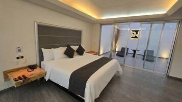 Camera d'albergo moderna con un letto grande, un comodino con il telefono e una porta scorrevole in vetro che dà su un balcone.