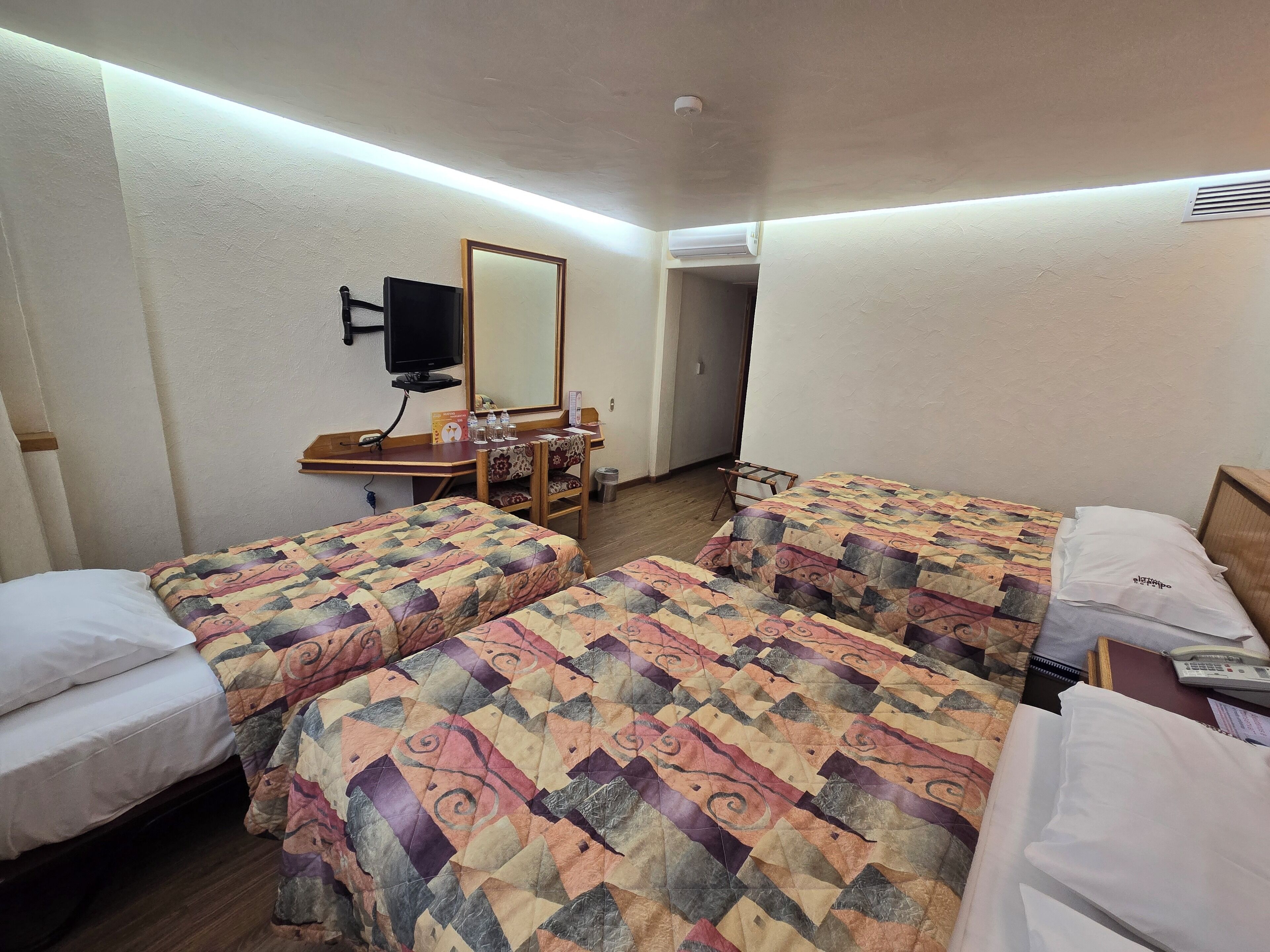 Una habitación de hotel con dos camas, un escritorio, una silla, un televisor y un espejo.