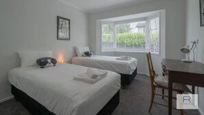 Une chambre avec deux lits, un bureau et une fenêtre avec des stores.