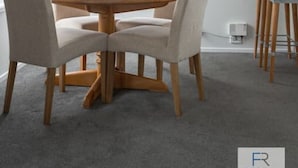 Un coin repas avec une table ronde en bois et quatre chaises, un tableau encadré au mur et une fenêtre avec des stores.