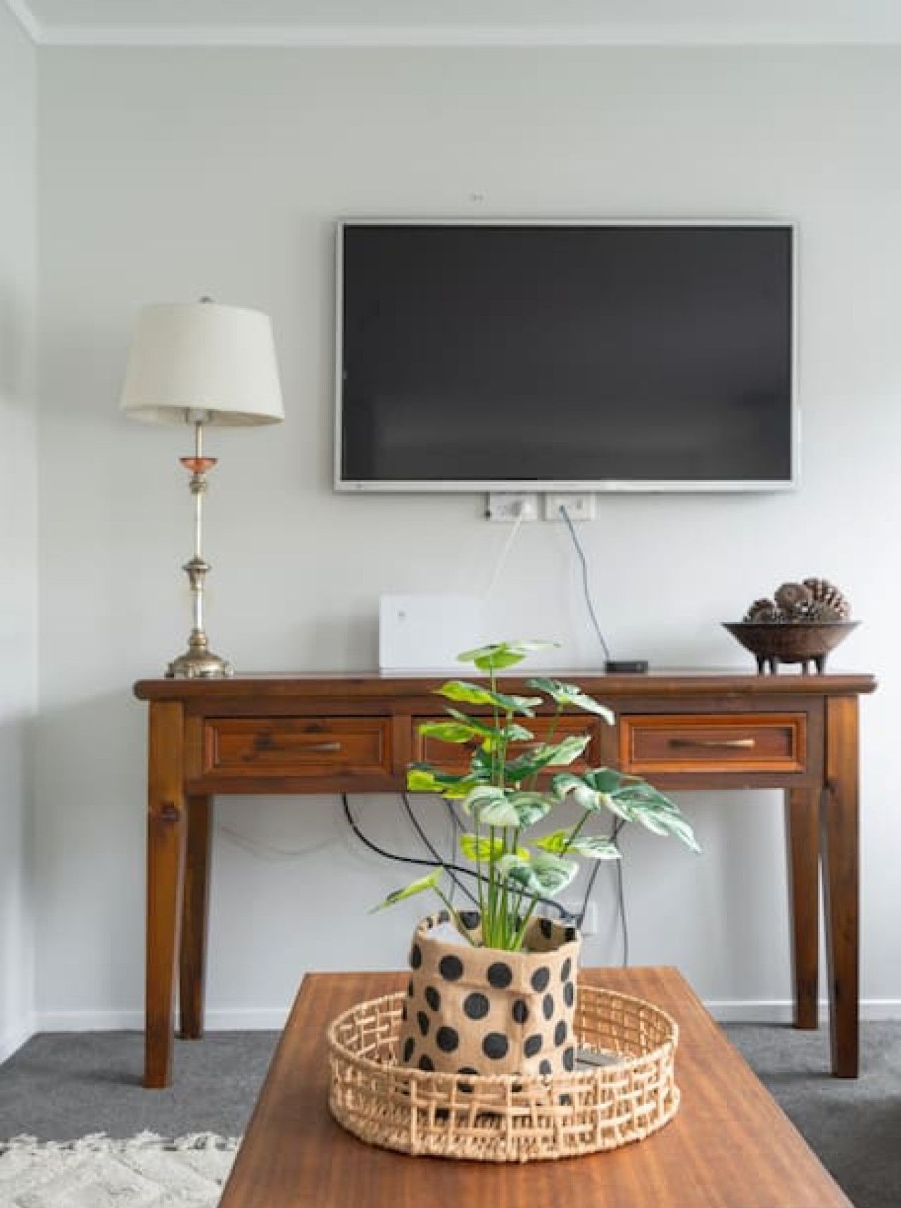 Un bureau en bois avec un téléviseur fixé au-dessus, une lampe sur le côté gauche et une plante dans un pot à pois posée sur le bureau.