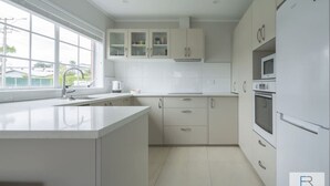Une cuisine moderne avec des meubles blancs, une grande fenêtre et un four à micro-ondes encastré.