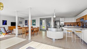 A modern kitchen with a central island, a dining area with wooden chairs, and a bar area with stools. - Stunning Poolside Residence| by Furnished Rentals (Auckland)