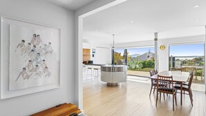 A modern kitchen with a central island, a dining area with a large table and chairs, and a view of the outdoors. - Stunning Poolside Residence| by Furnished Rentals (Auckland)