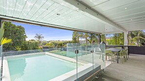 A rooftop infinity pool with glass railings, a dining area with chairs, and a view of the surrounding landscape. - Stunning Poolside Residence| by Furnished Rentals (Auckland)