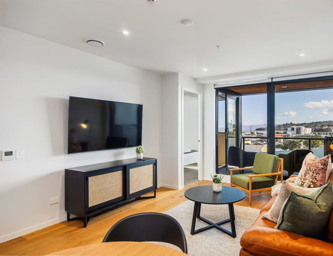 A modern living room with a large flat-screen TV, a black entertainment unit, a round coffee table, and a leather sofa.