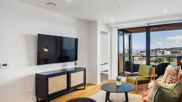 A modern living room with a large flat-screen TV, a black entertainment unit, a round coffee table, and a leather sofa.