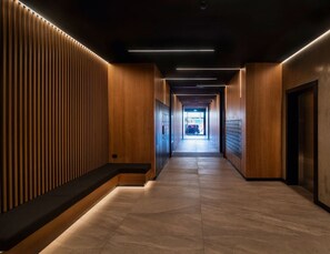 A modern hallway with wooden paneling, a tiled floor, and an elevator with a digital display. - Manukau Harbour Views| by Furnished Rentals (Auckland)
