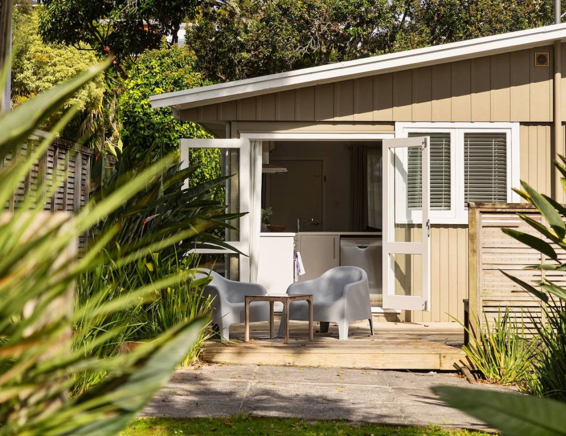 A small, single-story building with a patio area featuring two white plastic chairs and a table.
