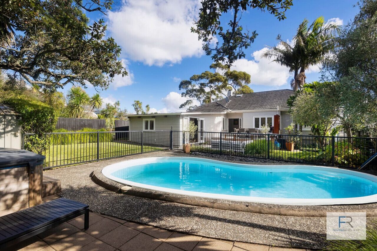 A residential property with a swimming pool, a fenced backyard, and a house with a tiled roof.