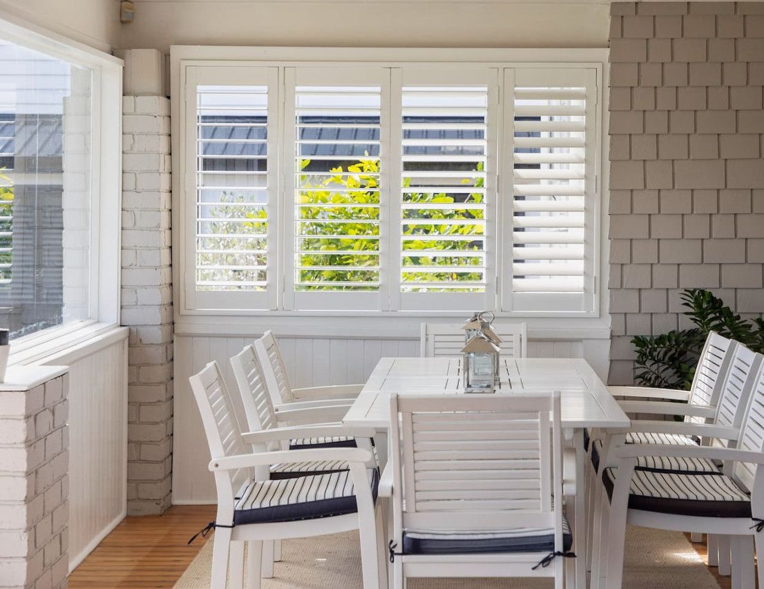A dining area with a white table and chairs, a brick wall, and a window with blinds.