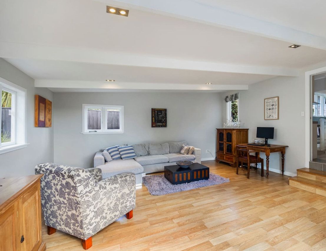 Een ruime woonkamer met een bank, een gestreept fauteuil, een houten salontafel en een kast.