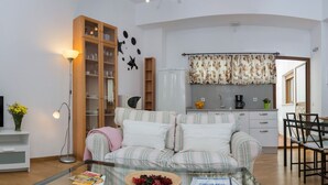 A living room with a sofa, a glass coffee table, a bookshelf, and a kitchen area with a refrigerator and a coffee machine. - DescubreHome Postigo, Inner Patio (Sevilla)