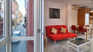 En moderne stue med en rød sofa, et glasbord og udsigt til en gade gennem en åben dør.