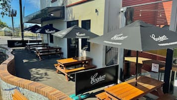 Outdoor seating with tables and umbrellas, a brick wall, and a building with a sign.