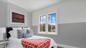 Ein Schlafzimmer mit einem Bett, einem Nachttisch, einem gerahmten Bild und einem Fenster.
