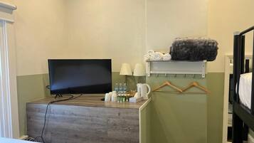 Een hotelkamer met een bed, een televisie, een bureau met een lamp, een koffiezetapparaat en een plank met handdoeken en een dekbed.
