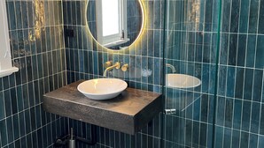 Ein modernes Badezimmer mit einem runden Spiegel, einem weißen Waschbecken und einer Duschkabine aus Glas.