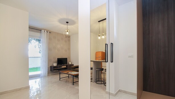A modern living room with a flat-screen TV, a sofa, and a coffee table. There is a dining area with stools and a small table. The room has a large window with curtains and a view of the outdoors. - Apartment 2355/115856 (Istria - Peroj), 1250m from the beach (Peroj)