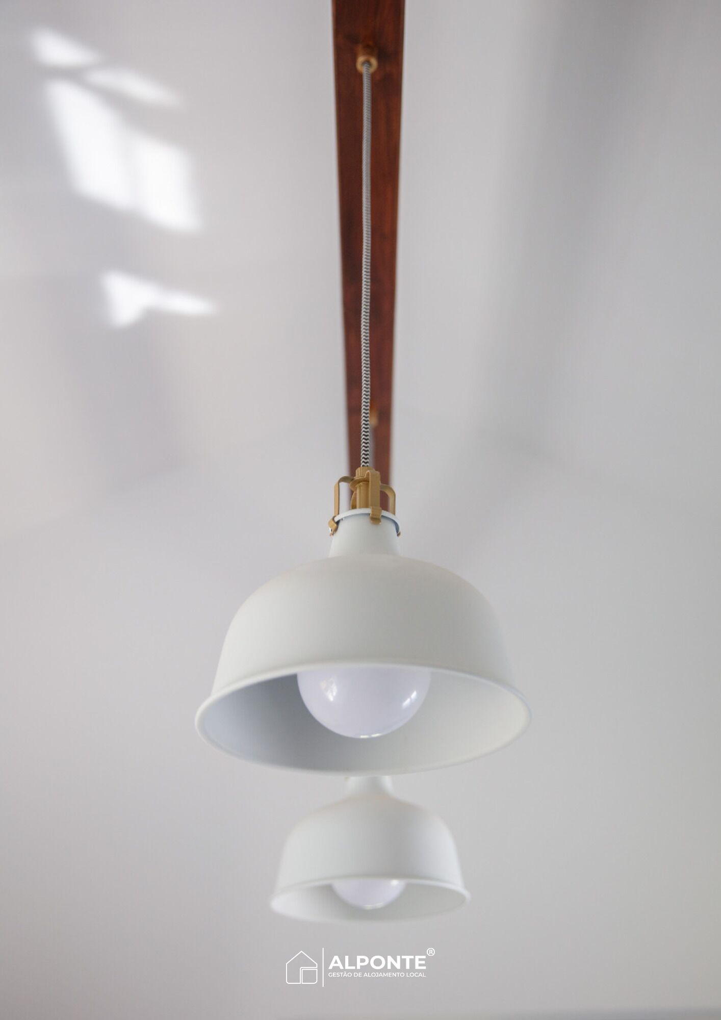 A pendant light with a white shade and brass accents, hanging from a wooden ceiling.