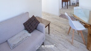A spacious living area with a wooden ceiling, a sofa, a glass table, and a kitchen in the background. - Quinta da Costeira - Casa Azul do Limoal (Arcos de Valdevez)