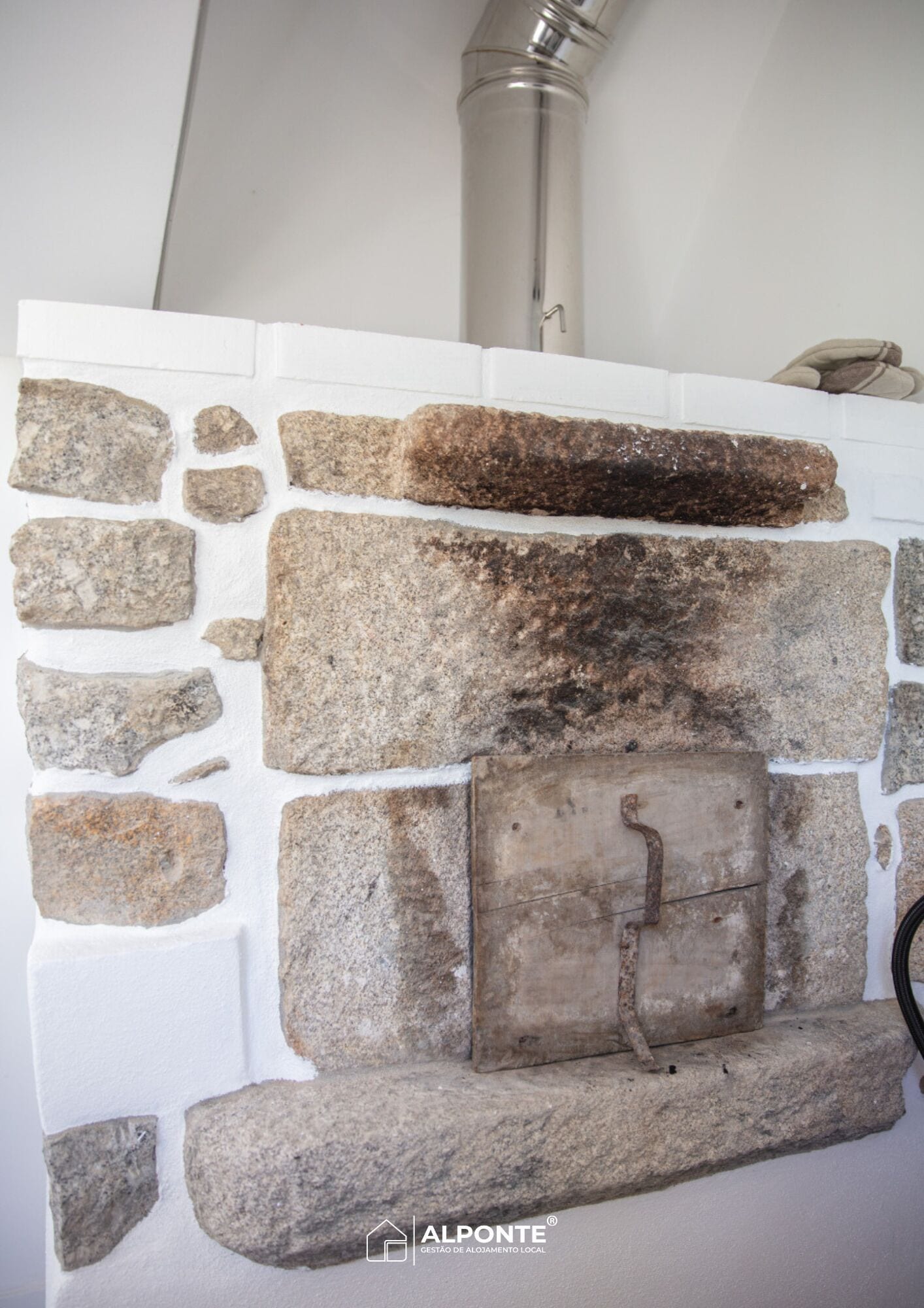 A stone fireplace with a metal grate, set in a white wall.