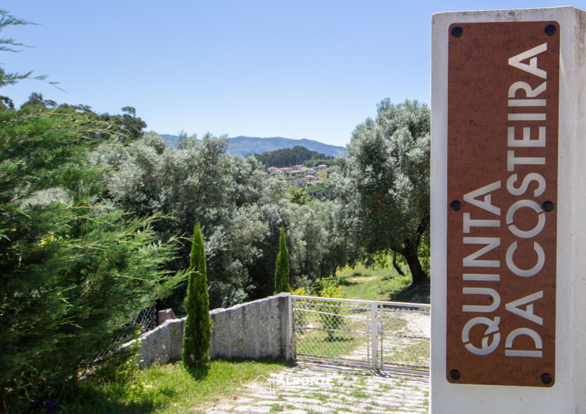 A sign reading "QUINTA DA COSTEIRA" with a view of olive trees and a distant town.